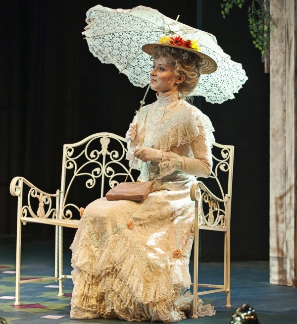 A lady in period clothing sitting on a garden bench holding a parasol